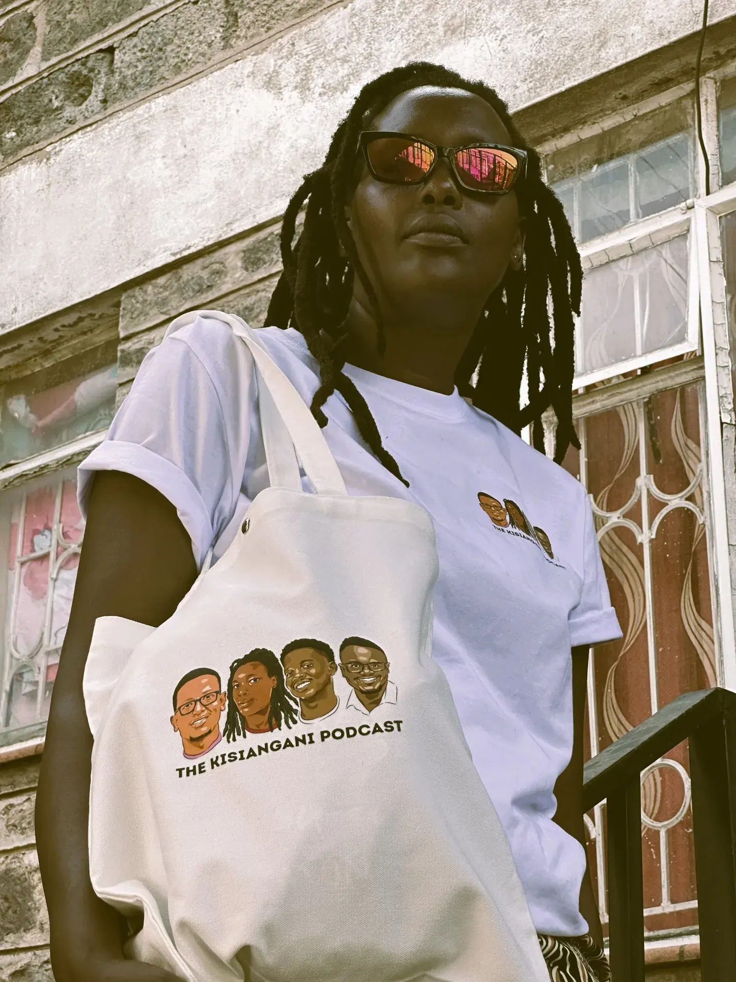 A tote bag printed with the crew's faces, worn over a Kisiangani Podcast tee